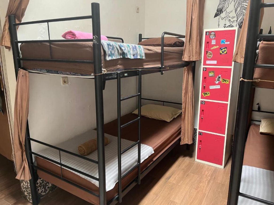 Air-conditioned mixed dorm with black metal bunk beds, privacy curtains and red lockers