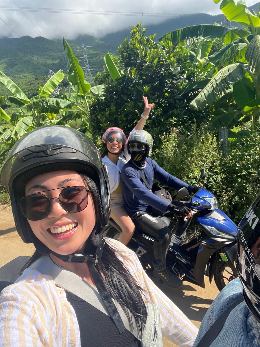 Smiling female rider in a helmet on a motorbike tour through green countryside