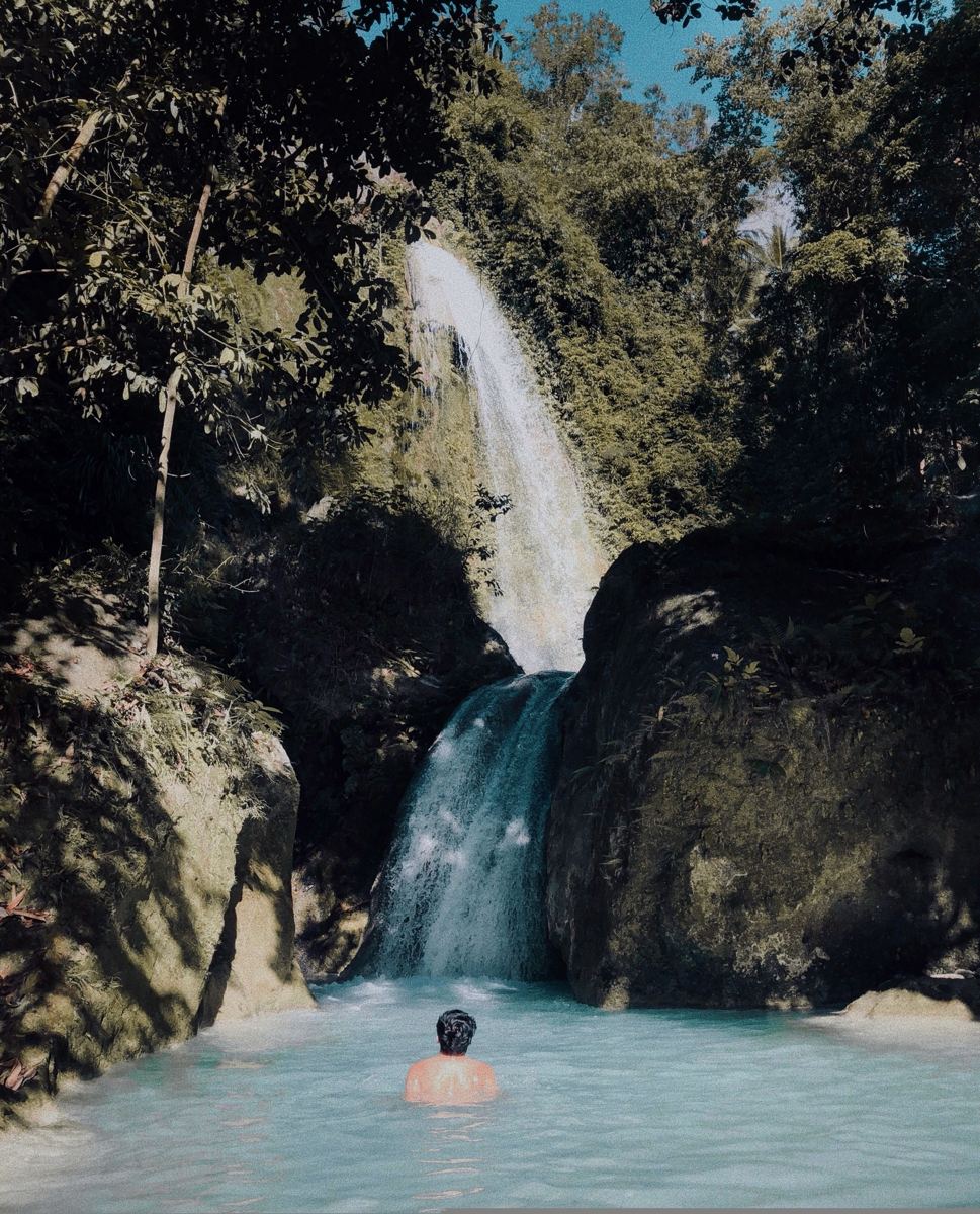 Swimmer in the turquoise pool below a jungle waterfall near Yogyakarta